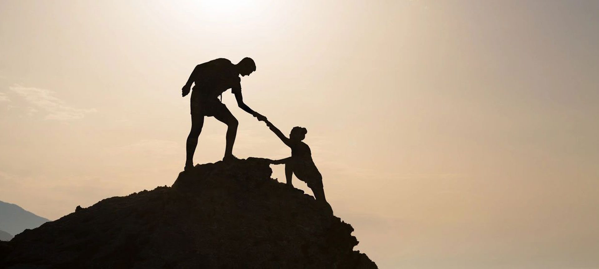 A man helping another person climb up the side of a mountain.